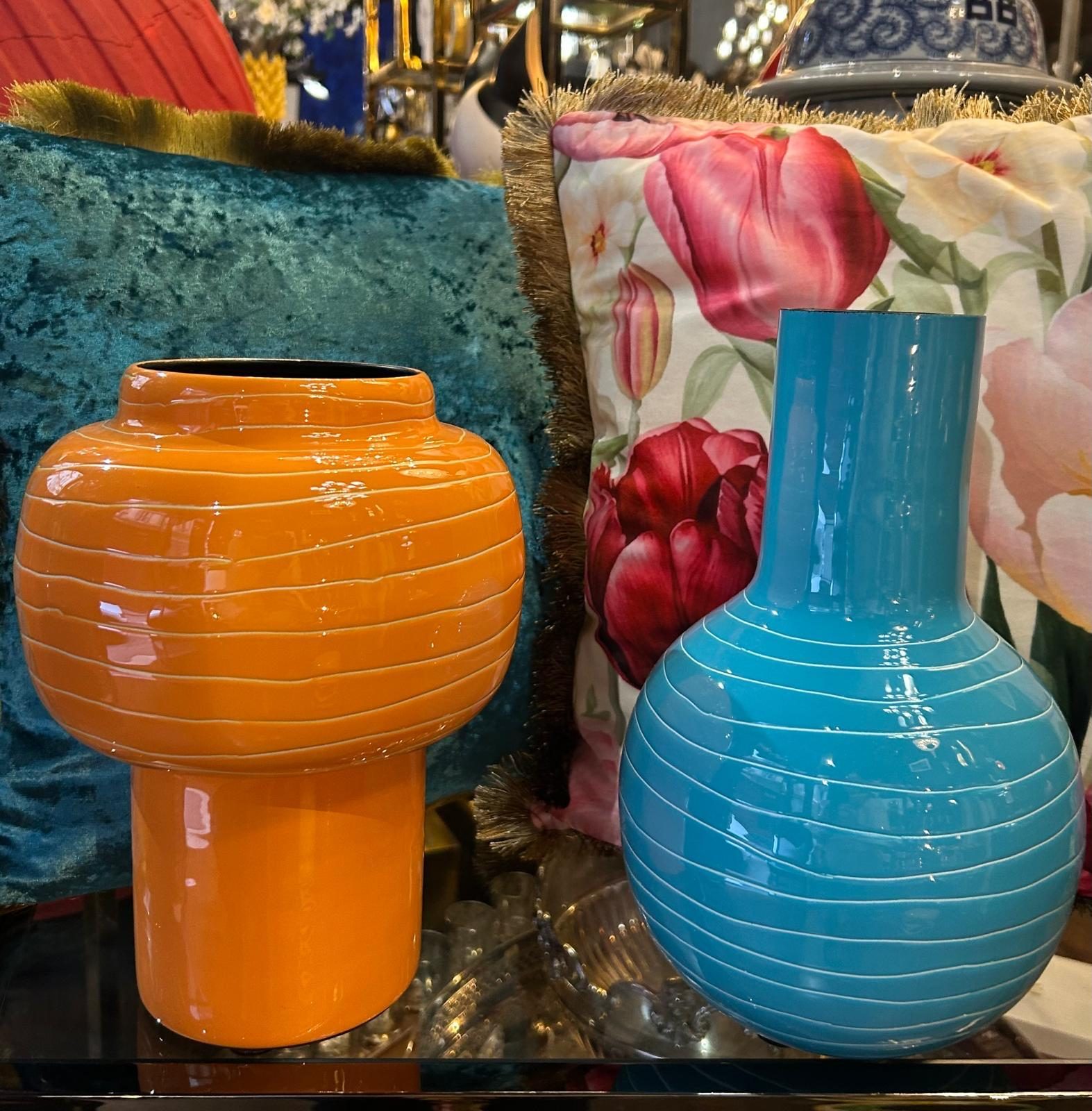 Vases en verre soufflé orange et bleu devant un fond fleuri